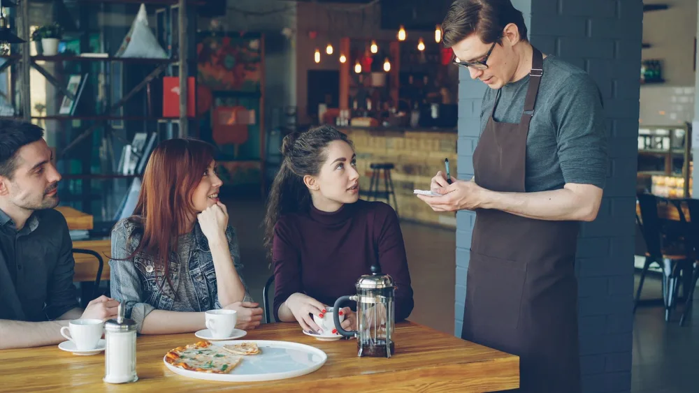 Grupo de clientes fazendo o pedido a um garçom na mesa de uma cafeteria